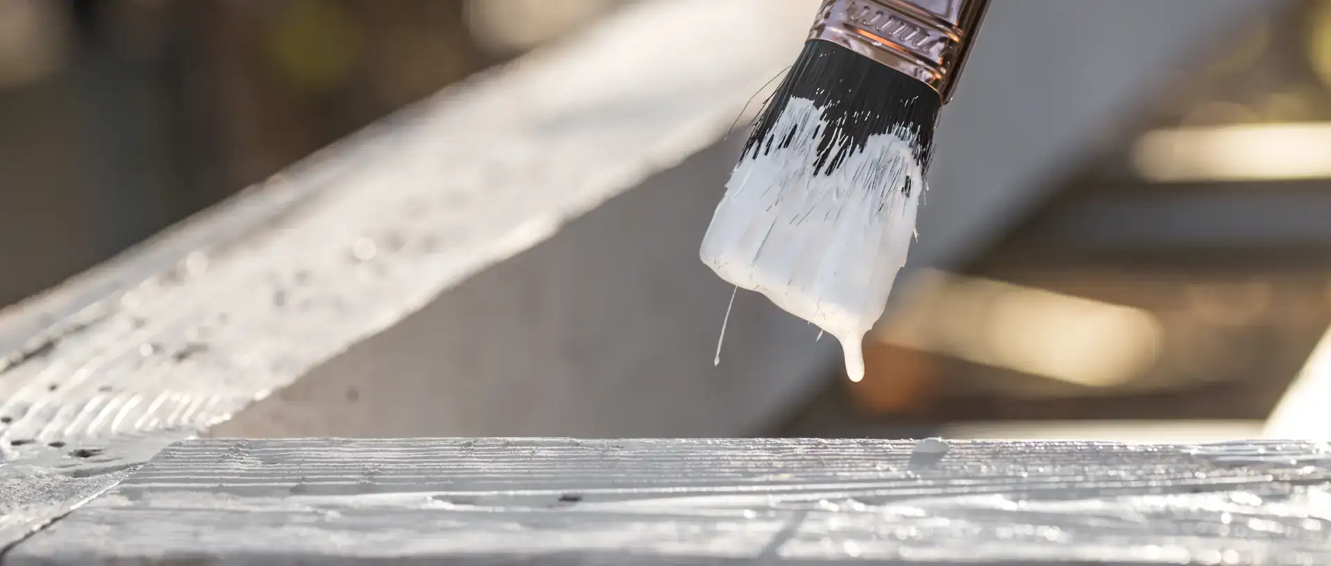 Billedet viser en pensel, der påfører maling på en træoverflade.