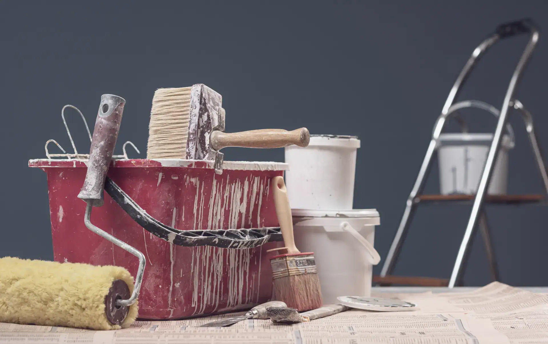 Malerudstyr med rulle, pensel og spand til malerarbejde.