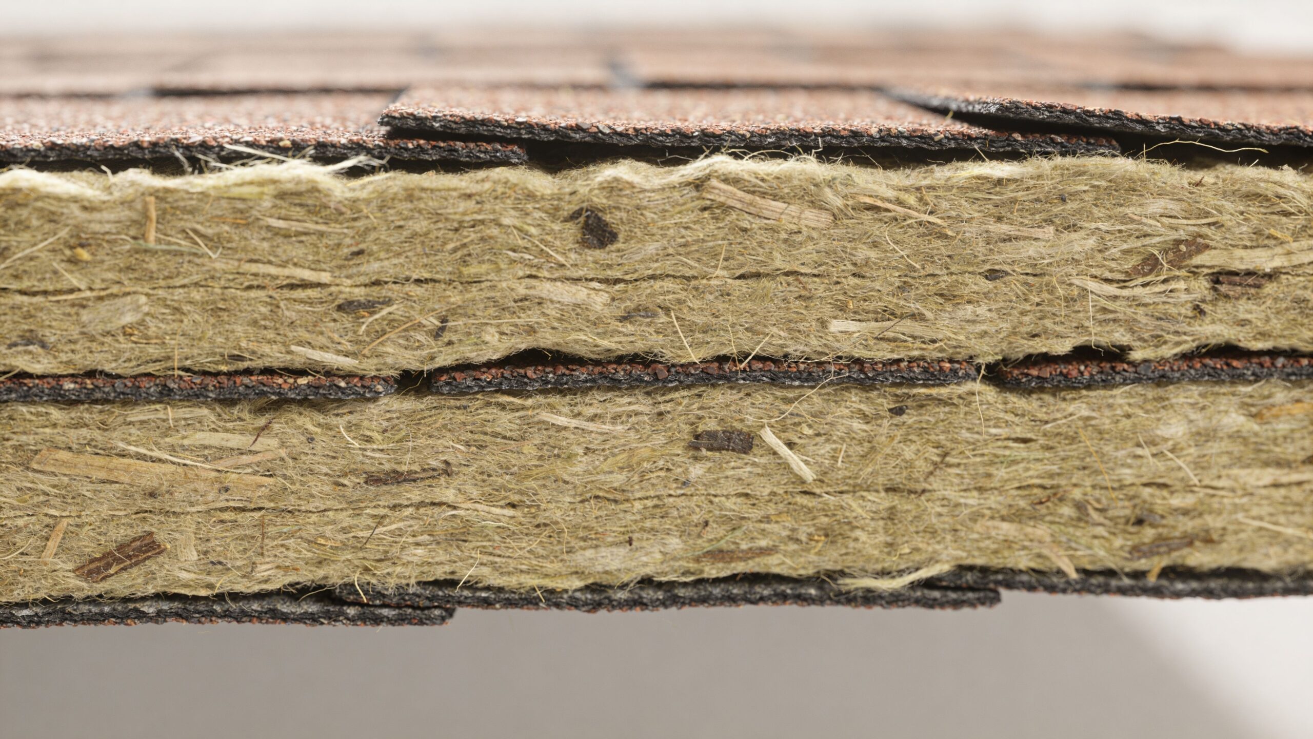 Et nærbillede af isoleringsmateriale med indlejrede fibre, der minder om asbest, placeret mellem lag af tagpap.
