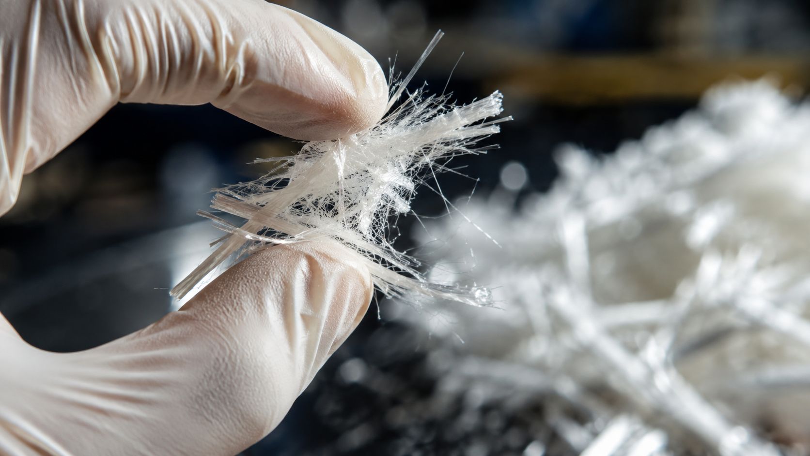 En person med handsker holder hvide asbestfibre mellem fingrene i et sikkert og kontrolleret laboratoriemiljø.
